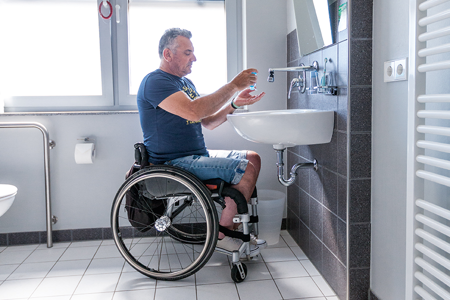 Mann im Rollstuhl am Waschbecken im Badezimmer